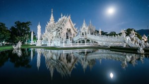 白色寺廟在明亮的月亮和星空下倒映在水中。