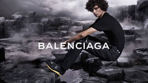 模特兒穿著 Balenciaga 服裝，坐在濕漉漉的火山岩上，背景霧氣瀰漫。 — 純黑色 壁紙