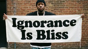 男人在磚牆前舉著寫有「Ignorance Is Bliss」的橫幅