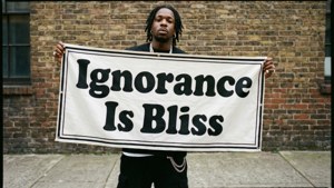 男子在磚造建築前舉著寫有「Ignorance Is Bliss」的橫幅。