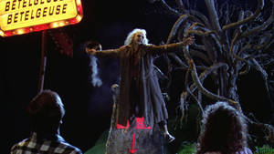Beetlejuice 站在發光標誌下的岩石上，身後有扭曲的樹木。