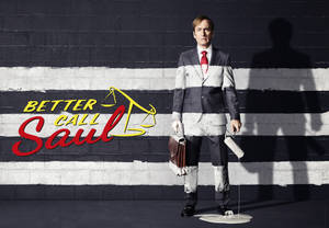 身穿油漆污漬西裝的男人，拿著公事包和油漆滾筒，站在帶有 Better Call Saul 標誌的條紋牆前。