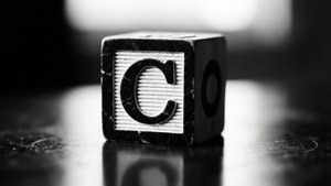 反光表面上的木製字母C積木，黑白。