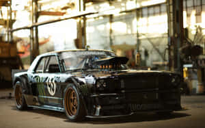 工業車庫內的黑色Hoonigan Mustang飄移車，金色輪圈。 — Steam Deck 壁紙
