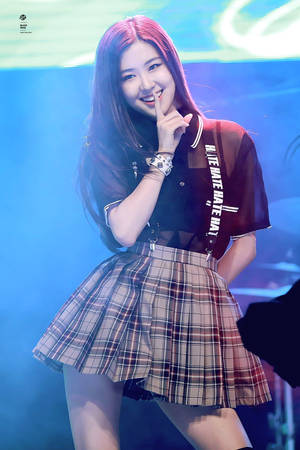 K-pop表演者在藍色燈光下的舞台上微笑並將手指放在嘴唇上。