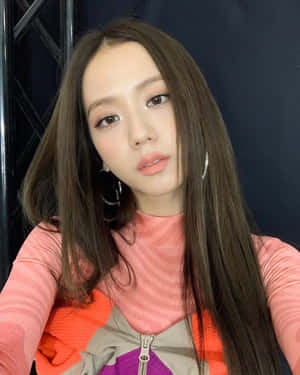 年輕女性，長長嘅棕色頭髮同圈形耳環，著住一件色彩繽紛嘅層次上衣。