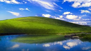 綠色山丘倒映在平靜的湖泊中，天空藍色，有白雲