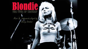 Blondie 在舞台上表演，身穿 Camp Funtime T恤，身後有鼓。