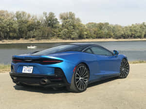 藍色McLaren跑車停泊在河邊，附近有樹木和小船。 — 4K 法拉利 壁紙