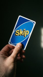 一隻手拿著一張藍色Uno Skip卡，上面有黃色文字。