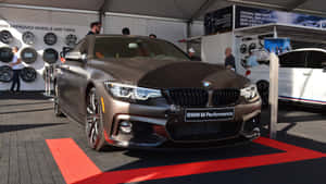 啞光棕色BMW M4雙門轎跑車在車展紅地毯上，背景有輪胎展示。