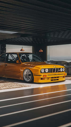 黃色BMW E30賽車在現代簡約的室內車庫中，配有拋光地板和吊燈。