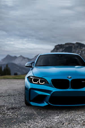 藍色BMW M2跑車停在礫石上，靠近山脈，天空多雲。