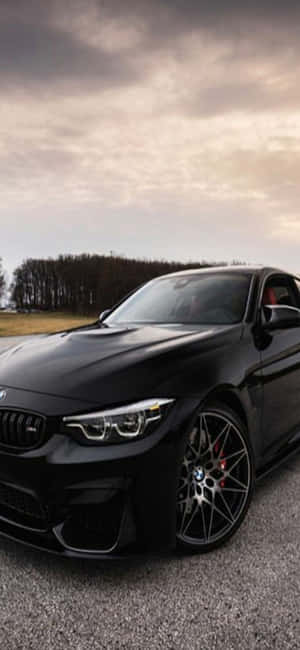 黑色BMW M4跑車停在碎石上，背景為多雲的天空。 — Infinix Note 60 Ultra 壁紙