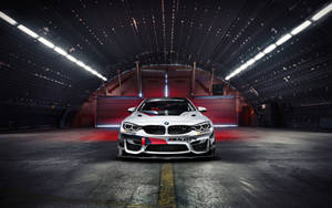 白色BMW M4 GT4賽車在黑暗的工業車庫中，頂燈明亮。