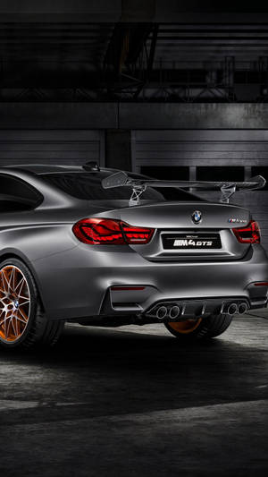 昏暗工業車庫中的啞光灰色BMW M4 GTS，配備銅色輪圈。