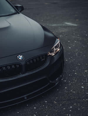 啞光黑色BMW M3跑車，金色頭燈，瀝青路面。