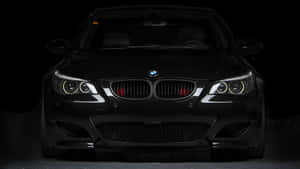 黑色BMW跑車正面視圖，車頭燈在黑暗的工作室中發光。