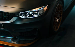 啞光黑色BMW M4，配金色輪圈和照明頭燈，在黑暗的工作室環境中。
