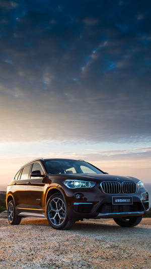 日落時分，碎石上的棕色BMW X1 SUV，車頭燈閃閃發光。
