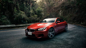 日落時分，紅色BMW M6轎跑車停泊在林間道路上。