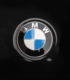 黑色汽車引擎蓋上的BMW標誌徽章，帶有鍍鉻飾邊和反射。 — Honor Magic V 壁紙