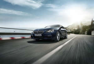 藍色BMW雙門跑車在海岸公路上疾馳，背景有海洋和山脈。