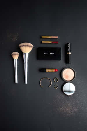 Bobbi Brown 化妝刷、唇膏和配件在深色背景上的扁平擺放。 — 化妝 壁紙