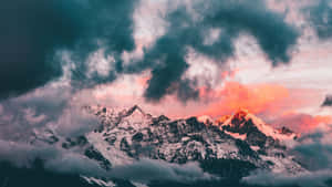 在戲劇性雲層下，充滿活力的日落天空下的雪山山脈。