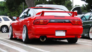 紅色日產Skyline R34跑車停泊在停車場，背景有樹木和其他汽車。