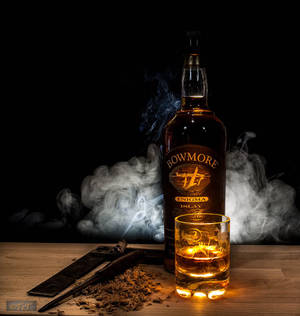 Bowmore 威士忌瓶和酒杯，帶有煙霧和雪茄剪在木桌上。