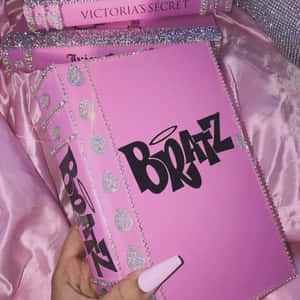 手拿著一本粉紅色閃粉Victoria's Secret Boatz書放在緞面布料上。 — 粉彩粉紅色 壁紙