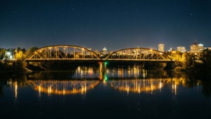 夜間河流上亮燈的桁架橋，城市天際線和星空倒映在水中