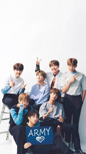 七位K-pop偶像在攝影棚中手持藍色ARMY標語牌擺姿勢。