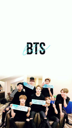七位K-pop偶像在明亮的房間裡手持標語牌，背景有BTS標誌。