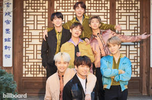 七位K-pop偶像在傳統木門前快樂地擺姿勢。