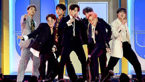七位男K-pop偶像身穿時尚西裝在明亮的燈光下於舞台上表演。