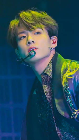 K-pop 表演者在藍色燈光下，以發光的頭髮和閃閃發光的服裝在舞台上唱歌。
