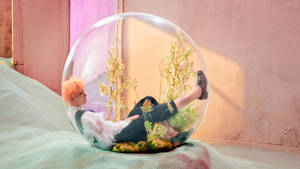 橙色頭髮嘅人喺床上一個裝有乾燥植物嘅玻璃球入面斜倚。