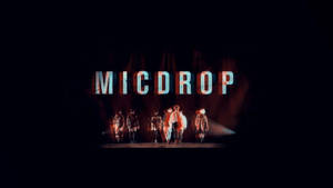 表演者在舞台上，下方是發光的MICDROP標誌，帶有紅色和藍色燈光。