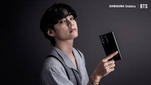 年輕男子在工作室環境中拿著黑色Samsung Galaxy手機。 — 三星 Galaxy S20 壁紙