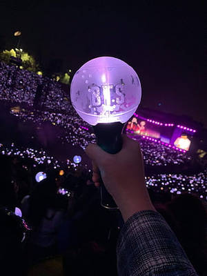 夜間演唱會中握著紫色BTS應援棒的手和粉絲人群。