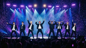 七位K-pop偶像在燈光閃耀的舞台上表演，五彩紙屑飄落，人群歡呼。
