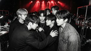 K-pop 樂團成員在紅色舞台燈光下聚集在後台。