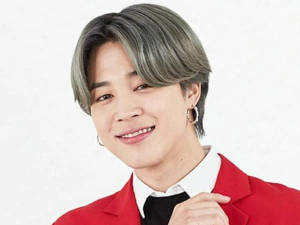 灰髮、戴著圈狀耳環的年輕男子身穿紅色西裝外套，對著鏡頭微笑。