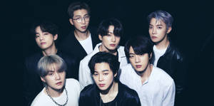 七位K-pop偶像身穿時尚服裝，在昏暗的攝影棚中認真擺姿勢。