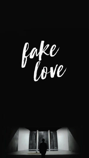 一個人在黑暗的房間裡獨自站在 'fake love' 字樣下方。