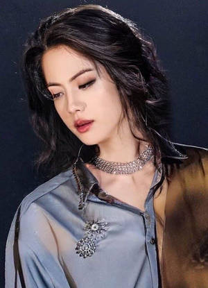 深色頭髮的女性在攝影棚中穿著藍色襯衫和閃亮珠寶。