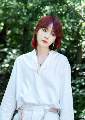 紅髮女性身穿白色服裝，站在陽光普照的森林中。