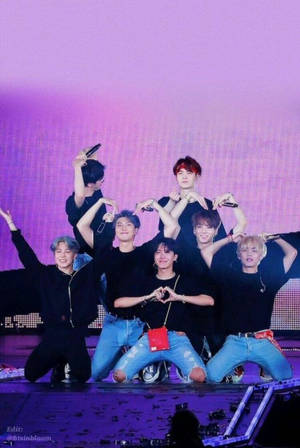 七位男K-pop偶像在紫色燈光舞台上擺出心形手勢。